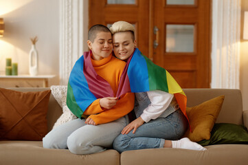Young freedom lesbian woman cuddling in lgbt rainbow flag while sitting on sofa