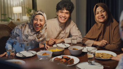 Happy Asian muslim family celebrate long distance with cousin use cell phone video call online Ramadan dinner together at home. Two generation celebration of Eid al-Fitr togetherness at home.