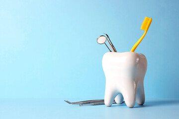Model of a human tooth with metal medical instruments for dental care and a yellow toothbrush on a blue background.
