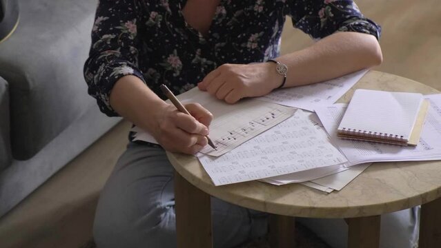 Caucasian female student rehearses, plays music and writes chords on paper, sitting on the floor at home.
