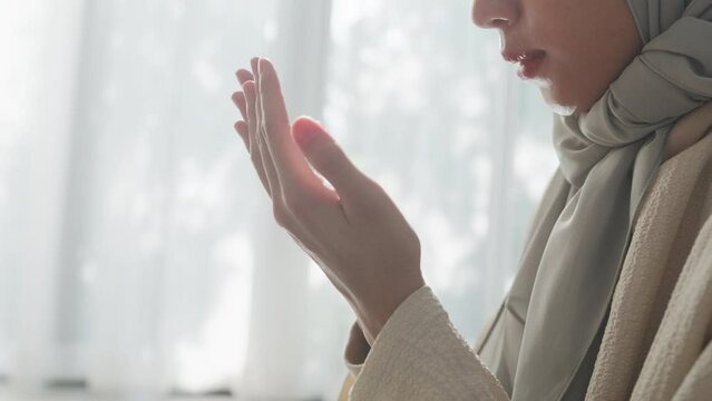 Close-up Asia muslim woman hand pray doa communicate to allah wear prayer clothes green mukena cover hijab in living room at home, pray room bright light, Islamic faith, Ramadan Kareem, Eid Mubarak.