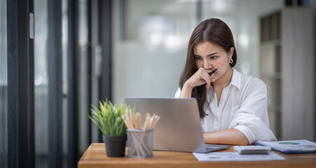 Portrait of tired young business Asian woman work with documents tax laptop computer in office. Sad, unhappy, Worried, Depression, or employee life stress concept
