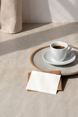 Coffee cup and blank paper card on beige table with aesthetic sun light shadow, minimalist neutral...