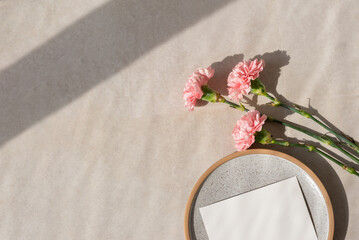 Elegant floral summer background, part of blank paper card on gray ceramic plate, carnation flowers...