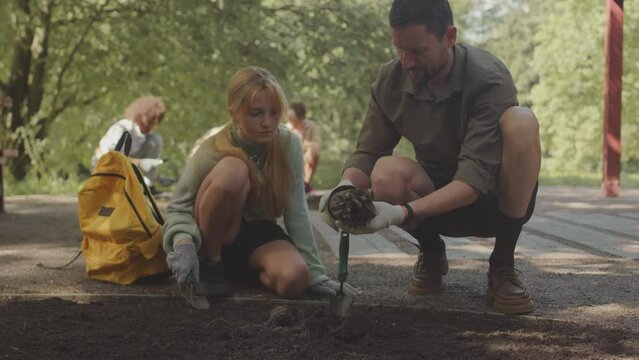 Male ranger showing preteen volunteer girl how to plant tree in public park on summer day
