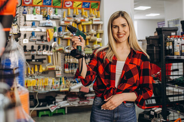 Beautiful smiling saleswoman is selling a drill at hardware store.