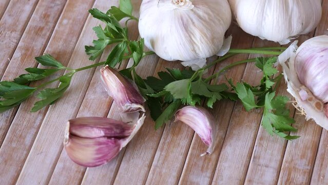 Unpeeled spicy garlic cloves and sprigs of fresh aromatic parsley on wooden cutting board. Cooking ingredients. Traditional condiments 