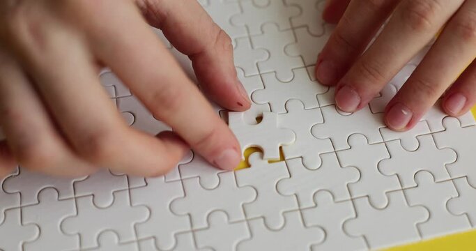Female hands insert missing piece into white puzzle on yellow background. Finding perfect business strategy. Successful combination of solutions slow motion