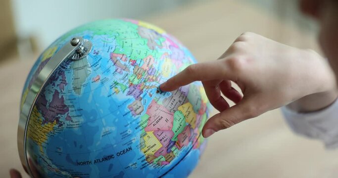 Schoolchild swipes finger over countries on globe in premise. Student studies Earth surface while gaining knowledge at school and dreams about travel abroad slow motion