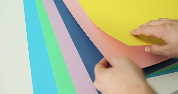 Interior designer examines sheets with color gamut samples for stylish apartment renovation. Hands of woman with colorful papers over white table