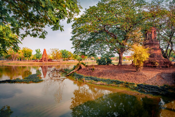 Fototapeta na wymiar Bright summer view of ruins of the ancient Buddhist temple Wat Phra Ram. Splendid morning scene of small pond with yellow water lilies, Ayutthaya, Thailand, Asia. Traveling concept background.