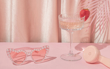 Summer creative layout with heart sunglasses, cocktail glass, phone handset and palm leaves with pastel pink curtain background. 80s or 90s retro aesthetic idea. Minimal summer fashion idea.