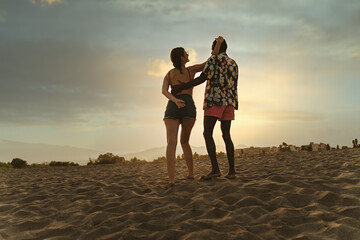 Young multiracial couple, Caucasian woman and African man, share intimate moment on beach at sunset. - Powered by Adobe