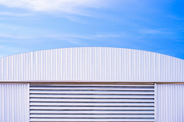 Aluminium louver on corrugated steel wall of warehouse building with curve metal roof against blue...