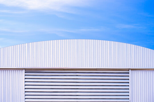 Aluminium louver on corrugated steel wall of warehouse building with curve metal roof against blue sky background