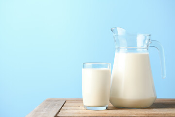 Glass and pitcher of fresh milk on wooden table with light blue background. - obrazy, fototapety, plakaty