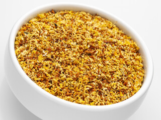 Close-up of dried osmanthus flowers in a white bowl on a white background. Side view, diagonal view. Herbal medicine. Therapeutic tea.