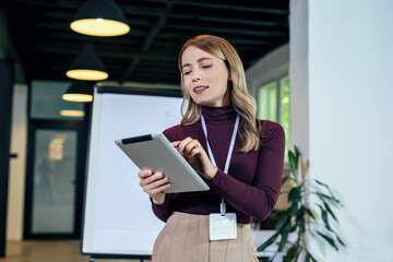 Smiling businesswoman standing in modern office with digital tablet.