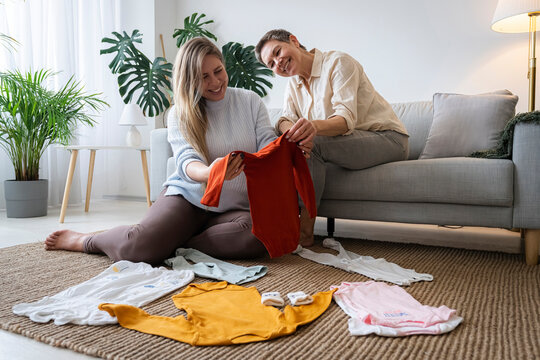 Mother and pregnant daughter looking at baby clothes sitting in living room at home