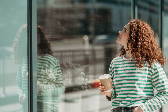 Young woman looking at glass wall holding disposable coffee cup