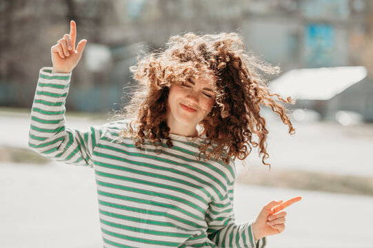 Smiling woman with curly hair dancing at sunny day