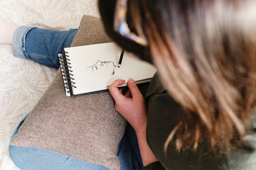 Woman sketching on spiral book at home