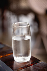 Water glass on wooden table with blurred background.