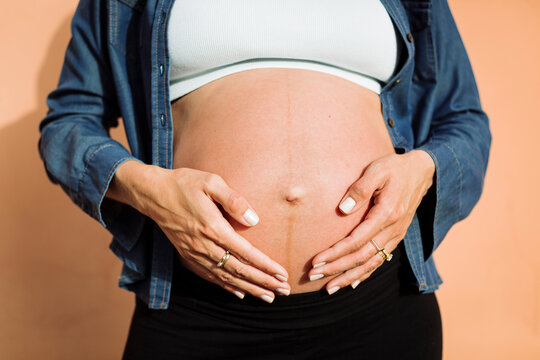 Pregnant woman with hands on stomach in front of wall