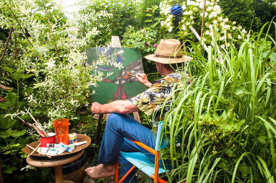 Man painting amidst plants sitting on chair in garden