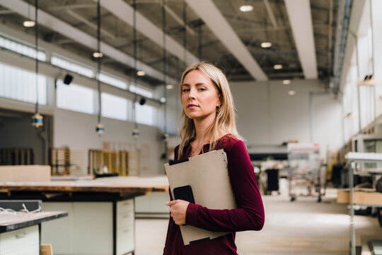 Confident businesswoman with blond hair holding file in factory