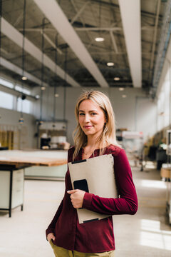 Smiling businesswoman with hand in pocket holding file in factory