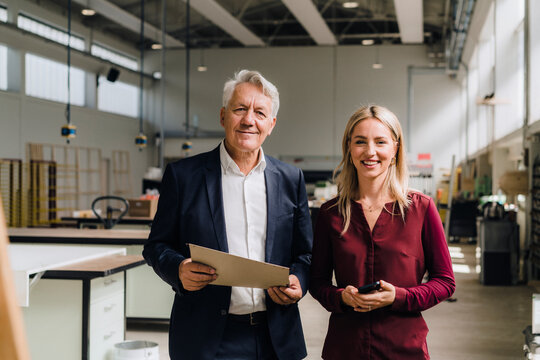 Smiling colleague with senior businessman holding document in factory