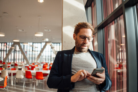 Businessman text messaging through smart phone at cafeteria