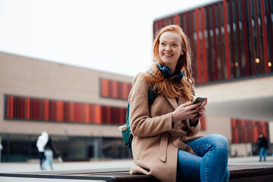 Smiling woman with smart phone sitting on bench