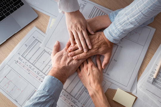 Business people stacking hands on desk with architectural plans