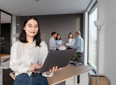 Portrait of young businesswoman using laptop with colleagues in background in office