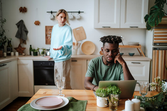 Woman arguing with man sitting with laptop in kitchen at home