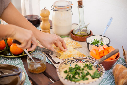 Hands cutting fermented bread surrounded with healthy meal in bowls and vegan products