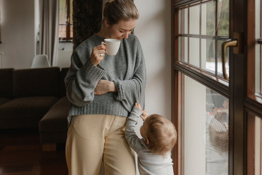 Son standing with mother holding coffee cup at home