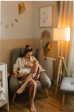 Mother breastfeeding baby girl sitting in armchair at home