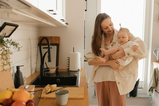 Smiling mother carrying daughter by kitchen counter at home