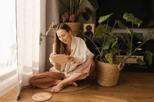 Young woman drawing on wood sitting in front of plants at home