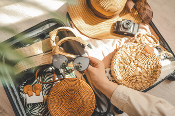 Woman hand holding sunglasses, hat, bag and other things on wooden table. Travel concept