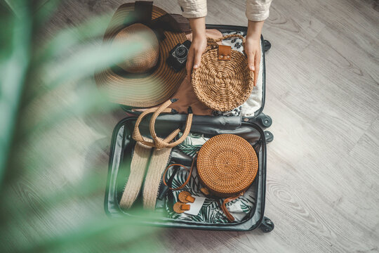 Top view of woman packing suitcase with hat, camera and bag for travel