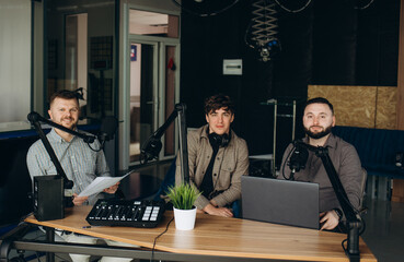 Side view of two radio hosts recording podcast in broadcasting home studio. Two cheerful radio...