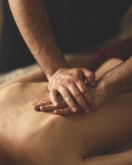 Woman is getting massage. Back massage. Dark-haired woman lies face down on couch. Masseur's hands on back. Relax, spa, body care. View from above. Soft focus.