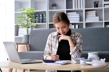 Asian businesswoman analyzing financial charts using laptop calculator and smartphone at office