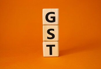 GST - Goods and Services Tax symbol. Concept word GST on wooden cubes. Beautiful orange background. Business and GST concept. Copy space.