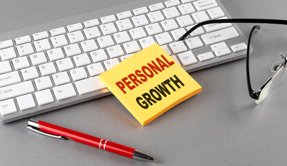 PERSONAL GROWTH text on a sticky with keyboard, pen glasses on grey background