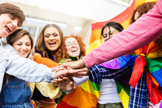 Young diverse group of friends celebrating LGBT pride day festival outdoors. Homosexual community people having fun stacking hands together showing freedom and unity. Lesbian, homosexual, transgender